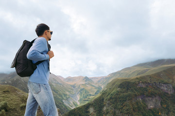 Young tourist man with a backpack against the background of the Caucasus Mountains, Georgia on a foggy day. copy space