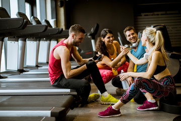 Fototapeta na wymiar Friends in sportswear talking and laughing together while sitting on the floor of a gym after a workout
