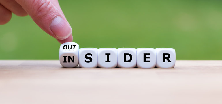 Hand turns a dice and changes the word "OUTSIDER" to "INSIDER" (or vice versa).