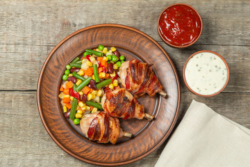 Fried chicken legs wrapped in bacon with vegetables. The view from the top. Copy-space.    