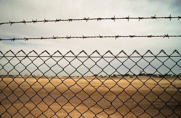 fence in the net with wire and barb. grey sky. fence in the desert.