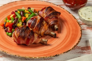 Fried chicken legs wrapped in bacon with vegetables