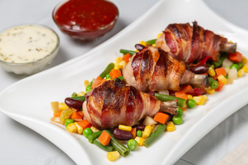 Fried chicken legs wrapped in bacon with vegetables