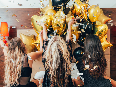 BFF Hangout. Urban Girls Leisure And Lifestyle. Glitter Confetti And Balloons Decor. Young Women In Black Relaxing On Bed.