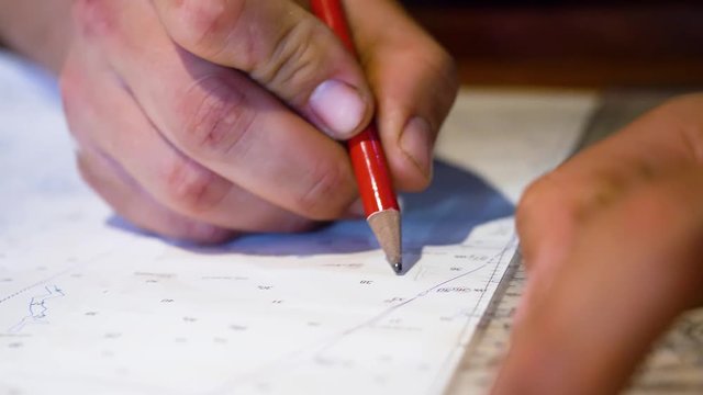 Close up of the Captain's hands using a pencil and protractor on a nautical chart at sea