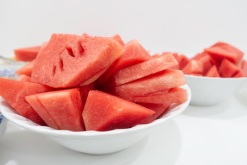 Pieces of watermelon in bowl and slice on white dish