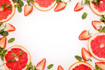 Cute flat lay with fresh fruit, sliced strawberry and grapefruit or red orange, mint leaves on white background.