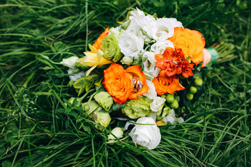Obraz na płótnie Canvas Beautiful wedding bouquet is lying in the grass. Engagement rings are on the flowers. Orange colours of fall and autumn in floral composition.