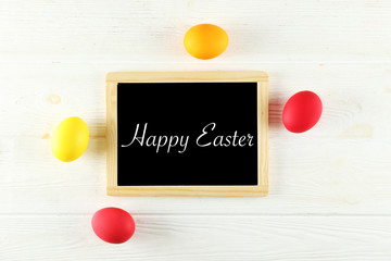 Blackboard with Happy Easter text, different colorful boiled paintd eggs. Greeting card concept with traditional holiday attributes. Wooden background, close up, top view, copy space, flat lay.