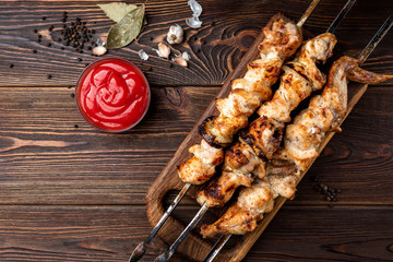 Grilled meat skewers, shish kebab with ketchup and spices on dark wooden background. Chicken shashlik.