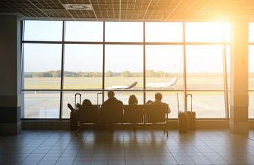 Tourists sitting in the airport with suitcases. People are waiting for the flight. Travel concept photo. Delayed plane.