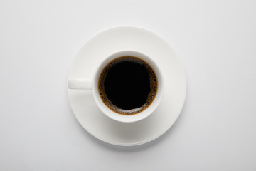 Top view of cup of black coffee and saucer on white