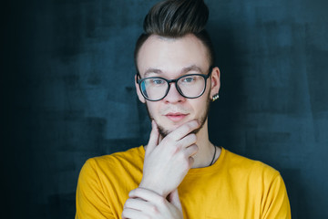 Portrait of curious hipster guy with comb over haircut. Young emotional man in glasses touching...