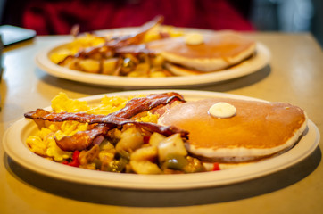 desayuno americano compuesto de tortitas, bacon, huevos, verdura, mantequilla y patatas.