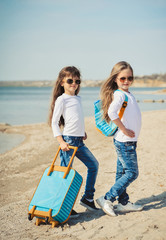Fototapeta na wymiar Cute little girls with suitecases on the beach are ready to travel. Summertime 