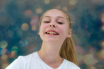 A concept portrait of a cute pretty blonde teen girl with long hair is sitting in a white T-shirt on a colorful background in the studio and talking.