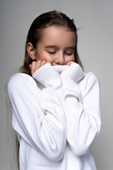 Portrait of a cute smiling teen girl wearing a white turtleneck sweater. Isolated on gray background. Advertising, trendy and commercial design. Copy space