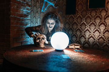 Scary witch with human skull over a crystal ball - obrazy, fototapety, plakaty