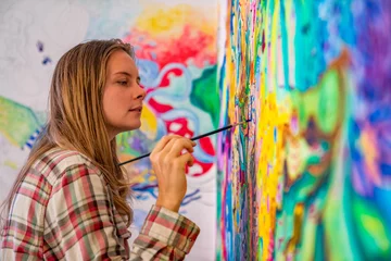 Fotobehang Joyful young female artist painting on the wall, using brush and bright acrylic paints © Alexander Zvarich 
