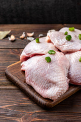 Raw chicken thighs on dark wooden background.