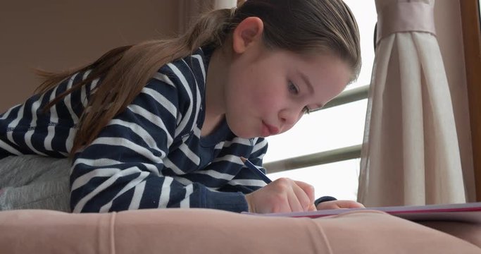 A pre-school girl drawing with pencils at home