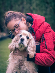 pretty teenage girl playing and kissing an american cocker dog in a park outside