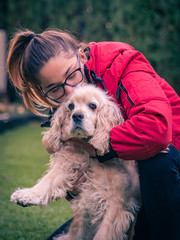 pretty teenage girl playing and kissing an american cocker dog in a park outside
