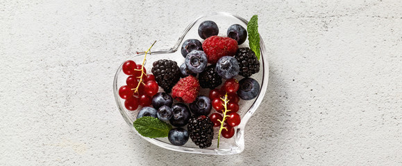 Fresh ripe berries in a glass heart-shaped bowl on a stone white table. summer season. healthy recipes and drinksrries in a glass heart-shaped bowl on a stone white table. summer season. 
