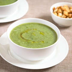 Fresh cream of zucchini soup with olive oil on top served in bowls, photographed with natural light (Selective Focus, Focus one third into the soup)