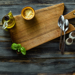 Cutting wooden board from olive wood on a blue wooden table with olive oil, basil and Parmesan cheese. Mediterranean table setting