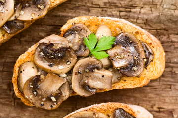 Fresh homemade mushroom and garlic bruschetta traditional Italian antipasto, photographed overhead on rustic wood (Selective Focus, Focus on the top mushroom slices)