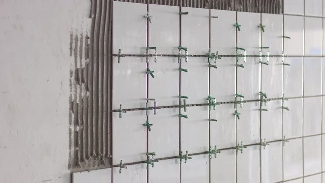timelaps how young woman put some white tile ceramic on grey cement on the wall. Tile work process. Tile aplication process