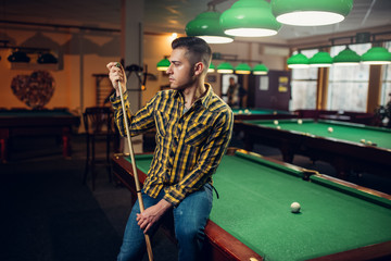 Male billiard player with cue poses at the table - obrazy, fototapety, plakaty