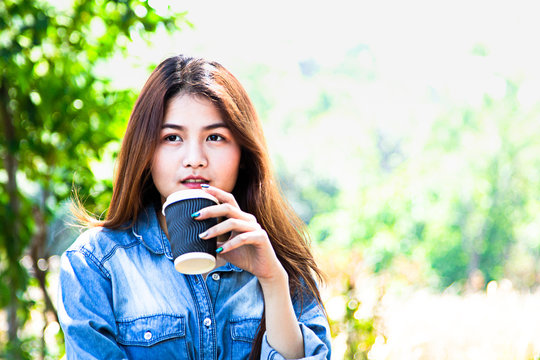 Asian Woman holding cup of takeaway coffee and looking at green forest in the nature park.