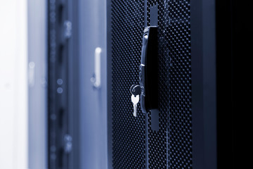 Close up meshed door with key in lock. Button in server room. Blur background of racks rows with...