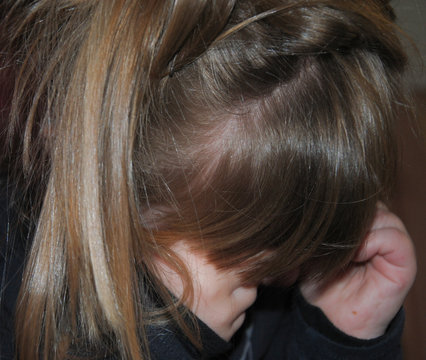 Ni&ntilde;a triste llorando con la cabeza agachada  frot&aacute;ndose los ojos
