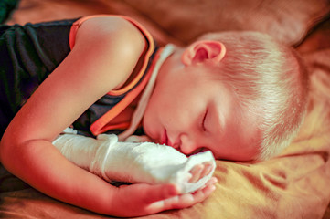 Cute kid is sleeping after medical procedures. His arm is bandaged and plaster cast on her.