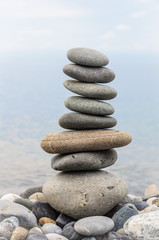 Fototapeta na wymiar Pyramid of sea stones on pebbles of the sea shore. Seascape. The concept of balance and spirituality.