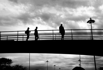 Silhouettes of group of unidentified people on the high bridge against cloudscape background