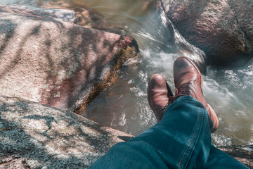 top view of feet with old brown shoes and blue jean on stone at the edge of the river
