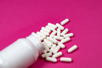White pills spilling out of a toppled white bottle 