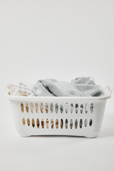 White plastic laundry basket with dirty clothes on grey