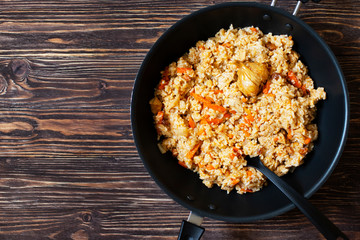 Traditional homemade Uzbek pilaf or plov in iron frying pan. Uzbek cuisine. Top view. Wooden background