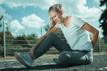 A young woman in sportswear is sitting on the sports field and looks painful