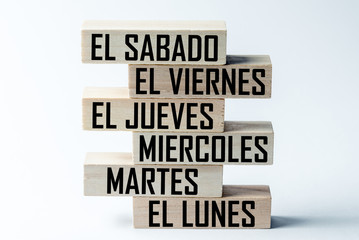 A list of wooden blocks lying on top of each other with a list of six-day working week days in Spanish, in the translation of the word: saturday, friday, thursday, wednesday, tuesday, monday