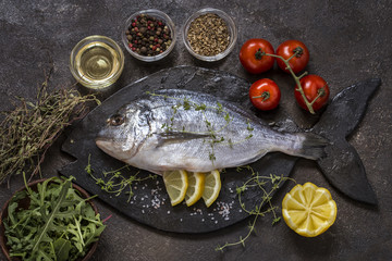 Dorado fish with fresh vegetables and herbs on a dark background