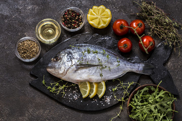 Dorado fish with fresh vegetables and herbs on a dark background