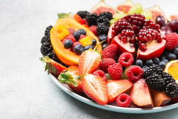 Delicious fruit platter pomegranate papaya oranges grapes berries on plate on white, selective focus