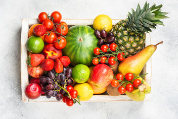Healthy raw rainbow fruits, mango papaya strawberries limes watermelon pineapple tomatoes in white box on light concrete background, top view, selective focus