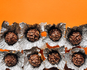 Spherical chocolates pralines are unfolded in foil wrappers. Top view. Orange background, copy space.